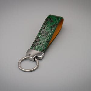 Peut inclure: Un porte-cl&eacute;s vert et noir &agrave; motif peau de serpent avec un anneau et une quincaillerie en m&eacute;tal argent&eacute;. L'int&eacute;rieur de la sangle est de couleur orange clair. Le porte-cl&eacute;s est un accessoire &eacute;l&eacute;gant.