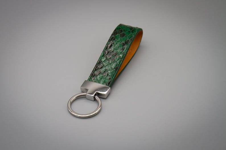 Peut inclure: Un porte-cl&eacute;s vert et noir &agrave; motif peau de serpent avec un anneau et une quincaillerie en m&eacute;tal argent&eacute;. L'int&eacute;rieur de la sangle est de couleur orange clair. Le porte-cl&eacute;s est un accessoire &eacute;l&eacute;gant.