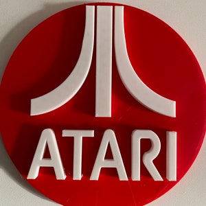 May include: A red circle with a white Atari logo. The logo features the classic Atari game console symbol and the word "ATARI" in white letters.