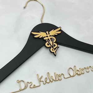 Può includere: Appendiabiti in legno nero con una targhetta in metallo dorato 'Dr. Kelvin Obina' e un simbolo di caduceo dorato.
