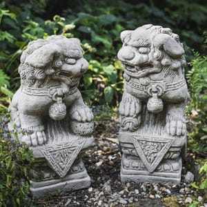 May include: A pair of grey stone Foo Dog statues with intricate details. The statues are standing on square bases with decorative carvings. Foo Dogs are a traditional Chinese symbol of protection and good luck.
