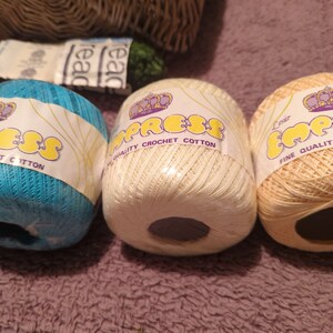 Puede incluir: Tres ovillos de lana en azul, blanco y amarillo. Cada ovillo tiene una etiqueta que dice "Empress Fine Quality Crochet Cotton".