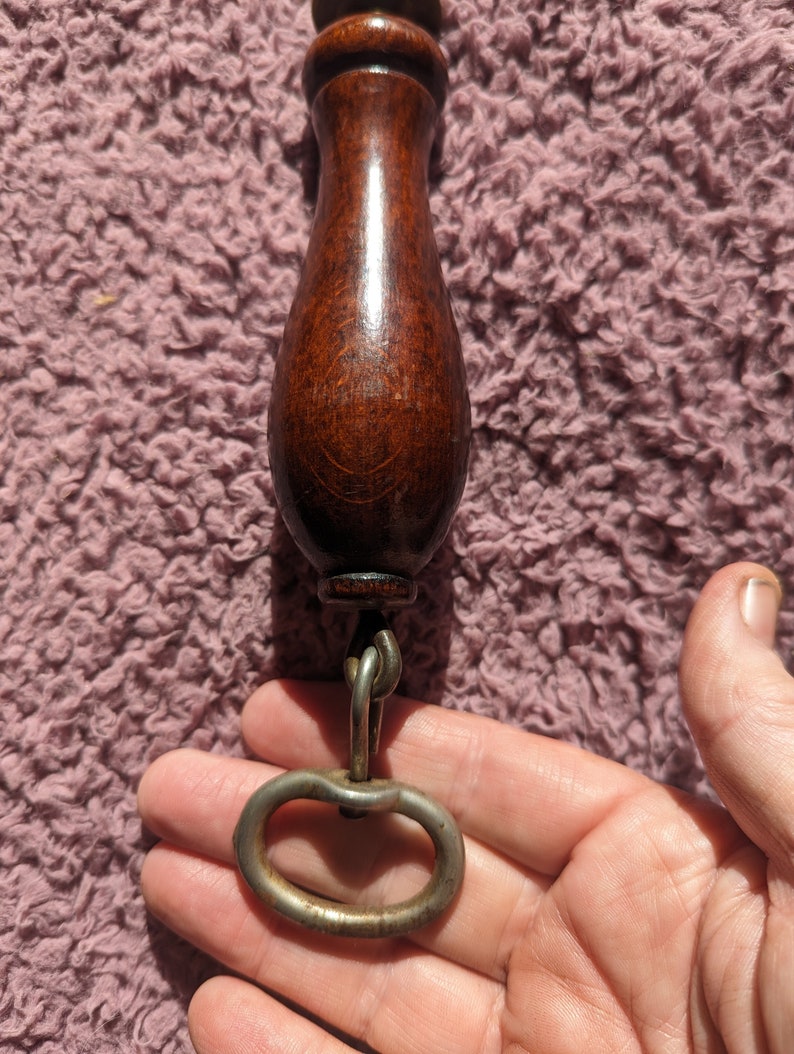 May include: A wooden handle with a metal ring attached to the bottom. The handle is dark brown and has a smooth finish. The ring is silver and has a simple design.
