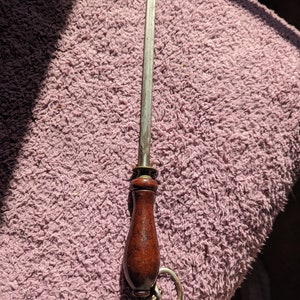 May include: A metal knife sharpener with a wooden handle and a metal ring attached. The sharpener is on a pink fuzzy surface.