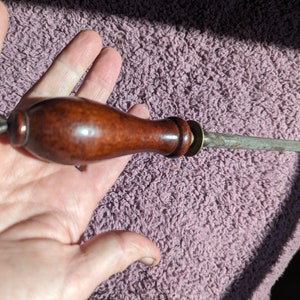 May include: A brown wooden handled steel knife sharpener with a metal ring and a chain attached to the handle.