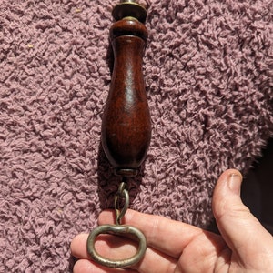 May include: A vintage knife sharpener with a wooden handle and a metal ring. The handle is dark brown and the ring is silver.