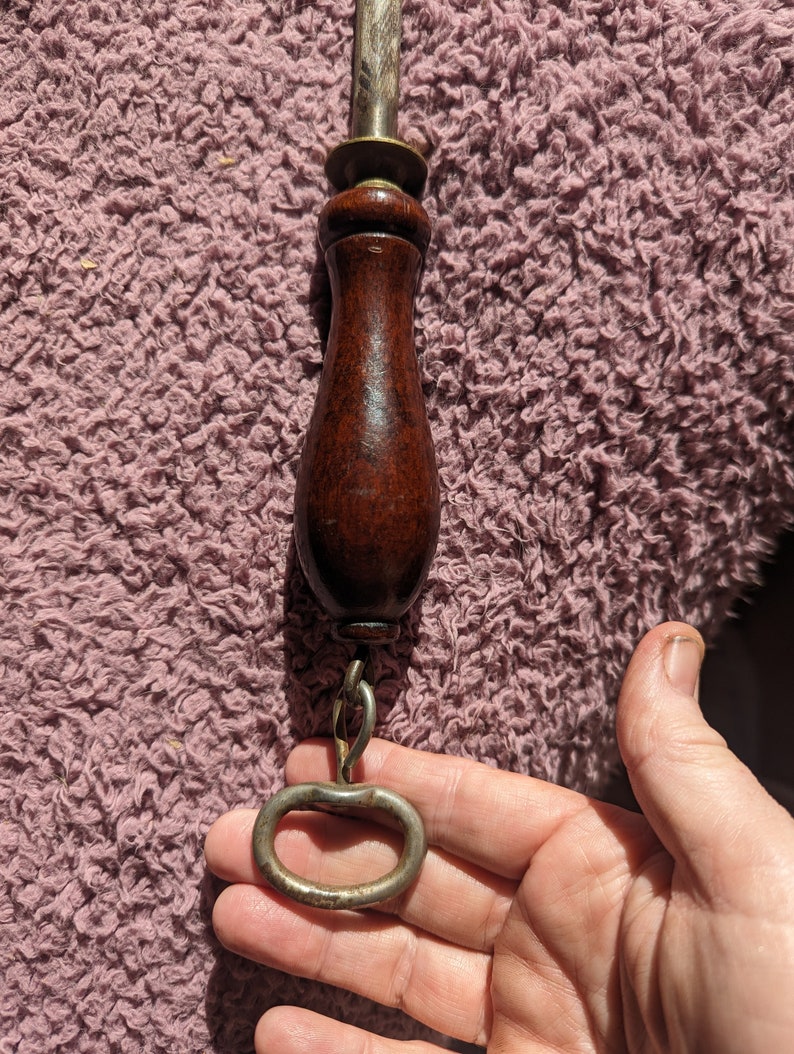 May include: A vintage knife sharpener with a wooden handle and a metal ring. The handle is dark brown and the ring is silver.