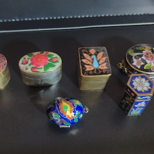 Puede incluir: Seis pequeñas cajas redondas decorativas con intrincados diseños florales. Las cajas están hechas de metal y tienen un acabado dorado. Los diseños están pintados en varios colores, incluyendo rojo, azul, verde y blanco.