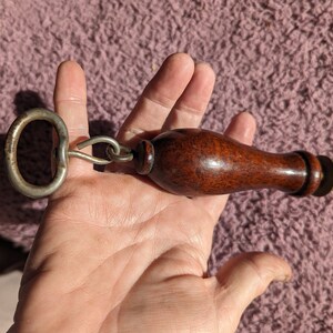 May include: A vintage knife sharpener with a wooden handle and a metal ring. The sharpener has a brass-colored metal base and a steel blade.
