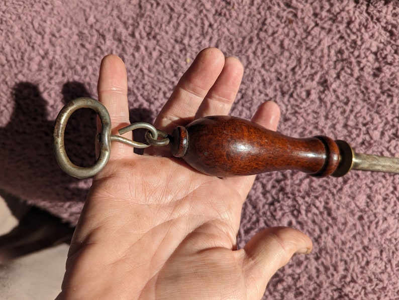 May include: A vintage knife sharpener with a wooden handle and a metal ring. The sharpener has a brass-colored metal base and a steel blade.