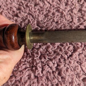 May include: A wooden-handled sharpening steel with a brass ring at the top. The steel is used to sharpen knives.