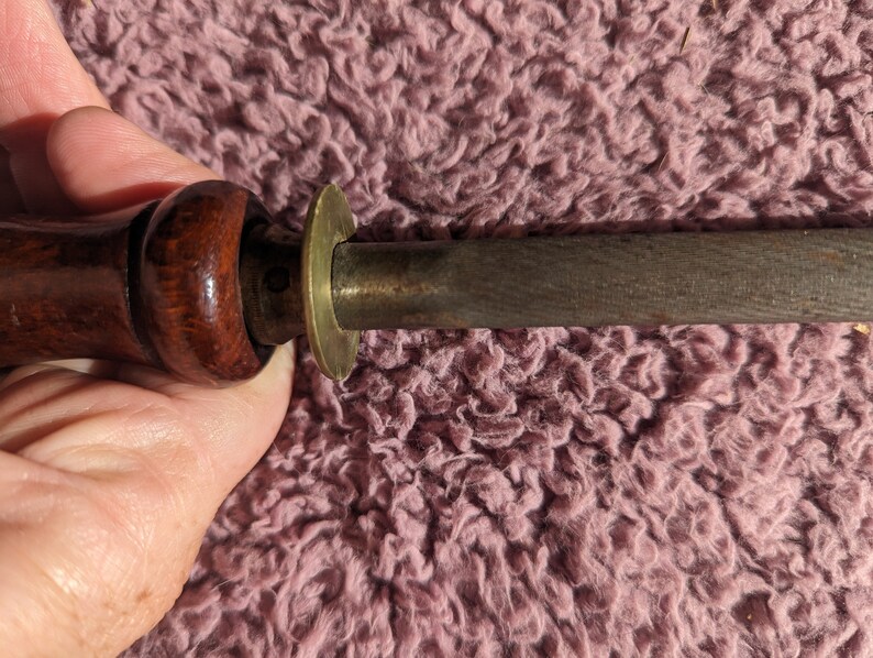 May include: A wooden-handled sharpening steel with a brass ring at the top. The steel is used to sharpen knives.