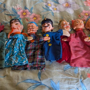 May include: A collection of seven vintage hand puppets. The puppets have painted faces and are dressed in various fabric outfits, including a devil, a policeman, and several characters in patterned clothing.