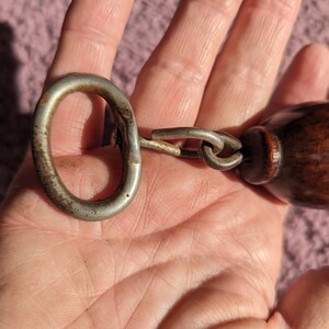 May include: A silver metal bottle opener with a wooden handle attached to a chain. The opener has a ring on one end and a bottle opener on the other end.
