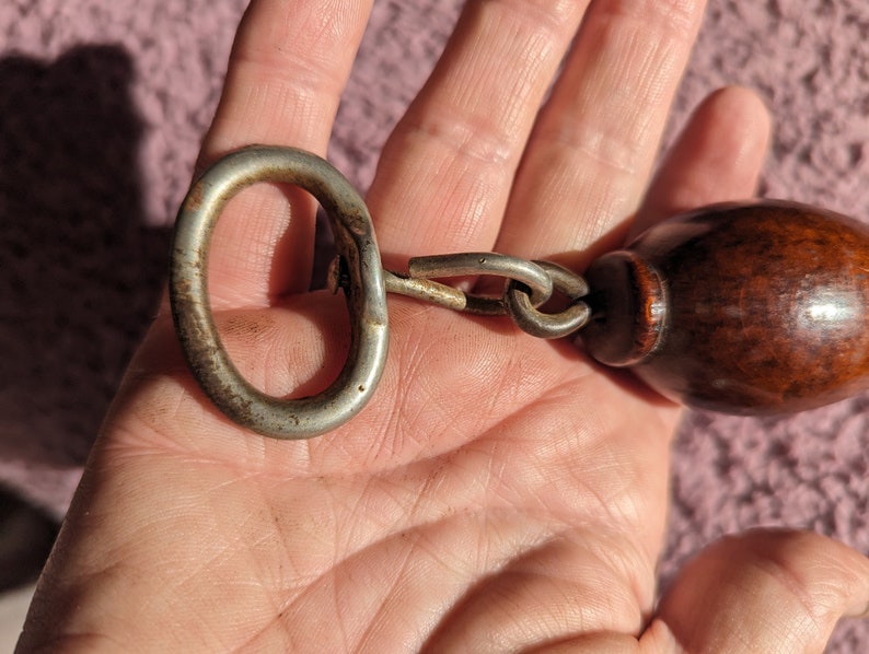 May include: A silver metal bottle opener with a wooden handle attached to a chain. The opener has a ring on one end and a bottle opener on the other end.