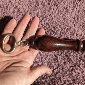 May include: A wooden handled tool with a metal ring and a sharp blade. The tool has a dark brown wooden handle and a silver metal ring.