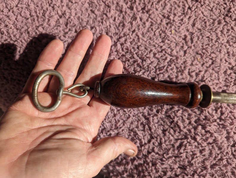 May include: A wooden handled tool with a metal ring and a sharp blade. The tool has a dark brown wooden handle and a silver metal ring.