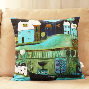 May include: Square decorative pillow with a whimsical landscape design. The pillow features a dark blue sky, light blue houses, and a black boat. The artwork uses shades of green, blue, and brown.
