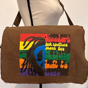 May include: A brown canvas messenger bag with a rainbow-colored graphic and the text "Freedom's just another word for nothing left to lose".