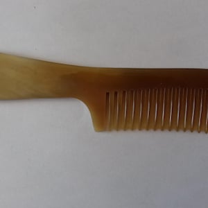 May include: A brown comb with a rounded handle and closely spaced teeth. The comb is made of a smooth, polished material and is designed for hair grooming. The handle is a lighter shade of brown than the teeth.