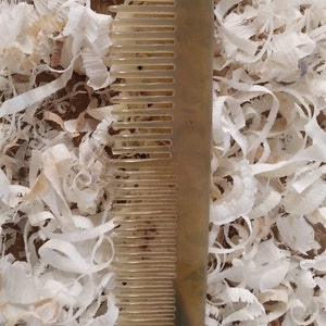 May include: A brown and tan comb with a fine-toothed design. The comb is made of a natural material and has a smooth, polished finish.