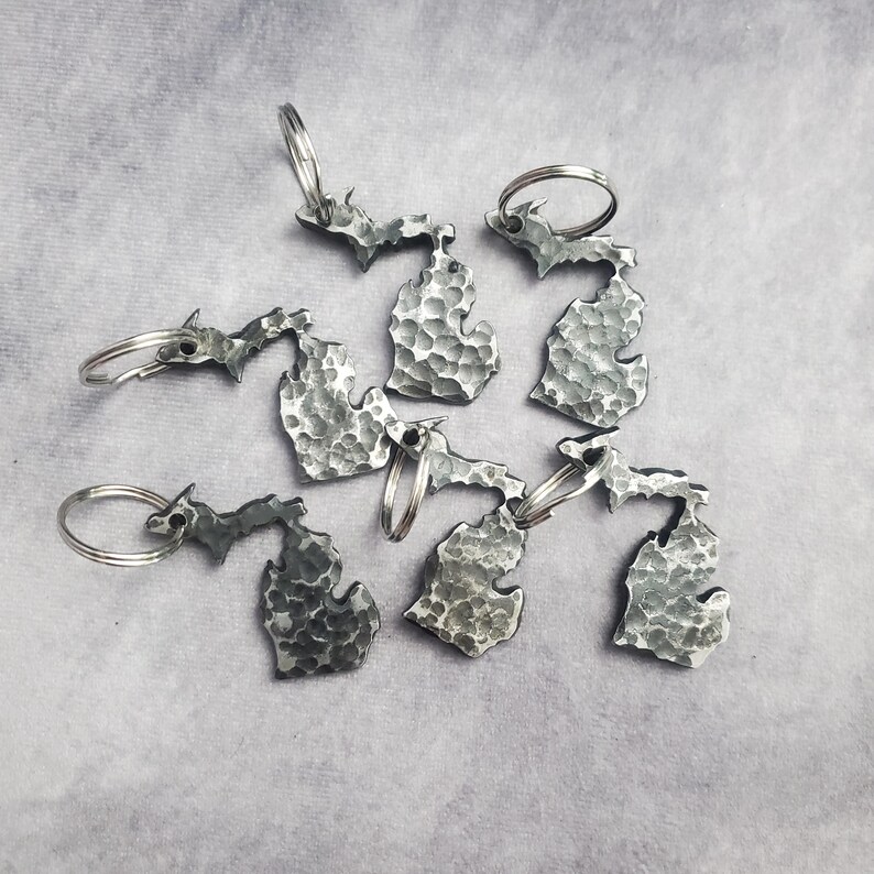 Puede incluir: Seis llaveros de plata con forma del estado de Michigan. Cada llavero tiene una textura martillada y un anillo de llave de plata.