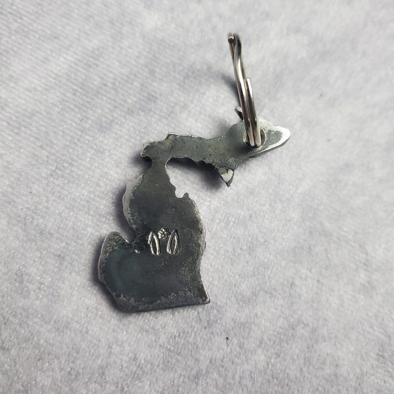 Puede incluir: Un llavero de metal plateado con forma del estado de Michigan. El llavero tiene un anillo en la parte superior y el n&uacute;mero "170" est&aacute; grabado en la parte inferior del estado.