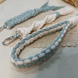 May include: Two keychains made of braided macrame cord. One is white and blue, the other is blue. Both have silver key rings.
