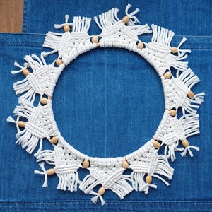 May include: White macrame wreath with wooden beads on a blue denim background.