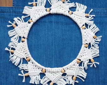 May include: White macrame wreath with wooden beads on a blue denim background.