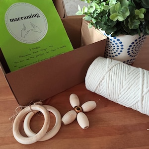 May include: A macrame plant hanger kit with three wooden rings, a ball of white cord, and instructions on a green card. The card says "macraming" and includes instructions for three models.