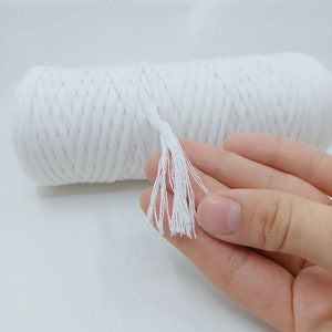 May include: A white cotton rope with a tassel on the end. The rope is rolled up and is being held by a hand.