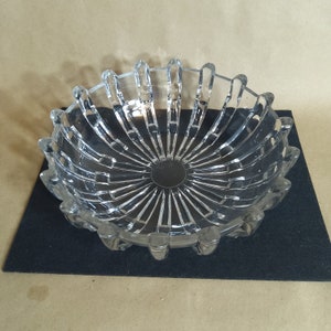 May include: A clear glass bowl with a decorative, radial pattern. The bowl has a scalloped edge and a slightly raised center.