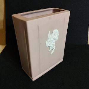 May include: A pale pink ceramic vase with a white floral design. The vase is rectangular with a square base.