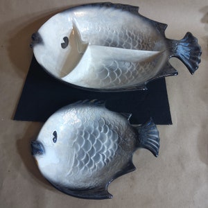 May include: Two ceramic fish-shaped serving dishes. The larger dish is divided into three sections and has a black and white glaze. The smaller dish is a single section and has a similar black and white glaze.