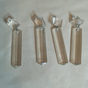 May include: Four clear glass crystal prisms with a pointed end and a square top. The prisms are hanging from a silver wire.