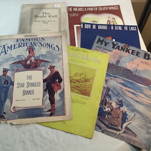 May include: A collection of vintage sheet music featuring patriotic songs, including "The Bugle Call", "The Star Spangled Banner", "My Yankee Boy", and "Seasons Go Rolling Along".