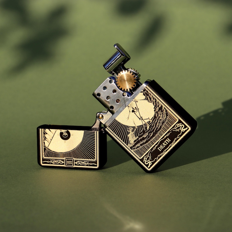 May include: A black and gold lighter with a design of the Death tarot card. The lighter has a wheel on the side and the words "Death" and "XIII" on the front.