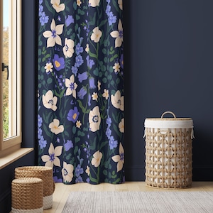 May include: A navy blue curtain with a floral pattern featuring white, blue, and purple flowers. The curtain is hanging in a room with a wicker laundry basket.