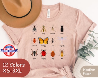May include: A heather peach t-shirt with a graphic of 12 different insects and their names. The insects include a fly, wasp, mosquito, beetle, cockroach, butterfly, ant, dragonfly, spider, ladybug, bug, and bee. The shirt is available in 12 colors and sizes XS-3XL. Made in the USA.