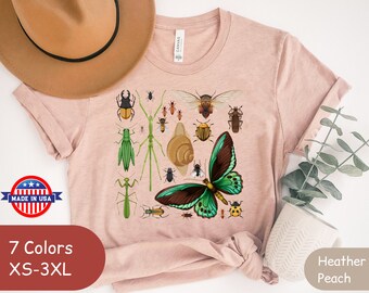 May include: A light pink t-shirt with a graphic print of various insects and a butterfly. The text "7 Colors XS-3XL" and "Heather Peach" are visible on the image.