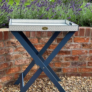 May include: A blue folding tray table with a white and blue patterned top. The table is sitting on a bed of small stones.