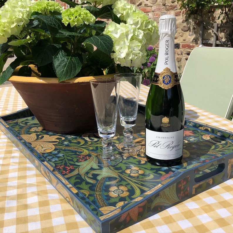 May include: A decorative serving tray with a floral design in shades of blue, green, and gold, holding two champagne flutes and a bottle of Pol Roger champagne. A large pot of green hydrangeas sits nearby.