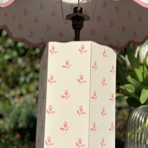 Op de afbeelding: Een witte tafellamp met een roze bloemmotief op de voet en een witte lampenkap met een roze gegolfde rand.