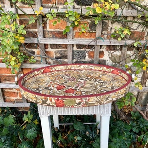 May include: An oval serving tray with a floral pattern in shades of red, green, and brown. The tray has a white wicker base and silver handles.