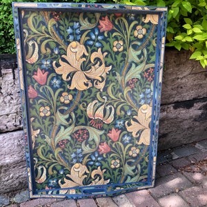 May include: Decorative serving tray with a dark blue frame and a floral pattern. The pattern features large yellow lilies, red and blue flowers, and green foliage on a dark background. The tray has a rectangular shape with curved handles.
