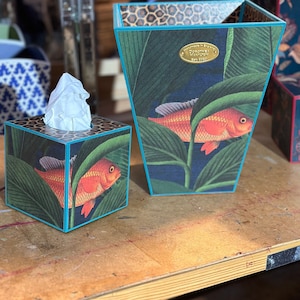 May include: Two decorative tissue boxes with a tropical fish design. The larger box is teal and features a gold label that reads "Handmade in England, Dorchester Pavilion, Est 1985". The smaller box is teal with a gold trim and features a single fish.