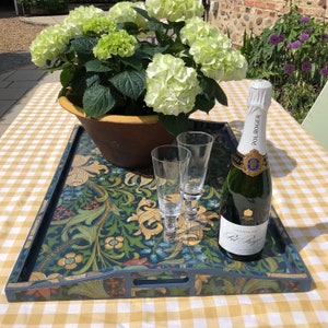 May include: A rectangular serving tray with a floral design in shades of blue, green, and gold. The tray holds two champagne flutes and a bottle of Pol Roger champagne. A potted hydrangea plant sits behind the tray.