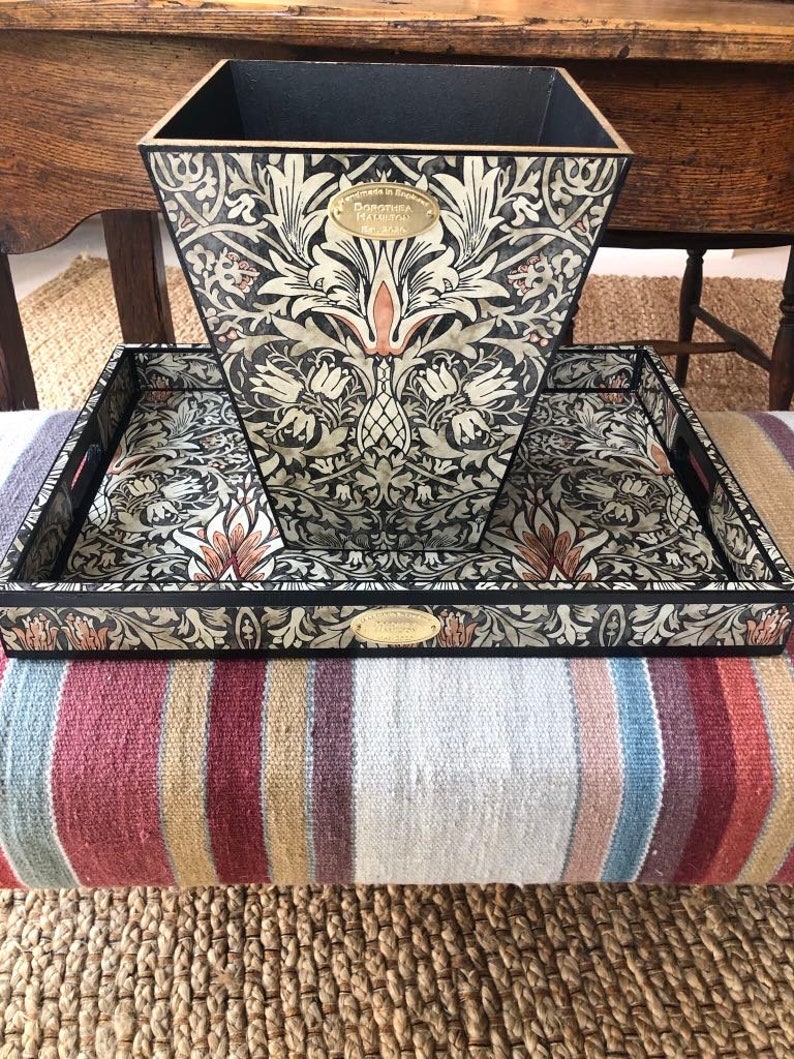 May include: A black and white tray with a floral design and a gold label that says "Made in England, Dorothea Harrison, Est. 1936". The tray is sitting on top of a black and white patterned wastebasket.