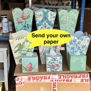 May include: A collection of six decorative tissue boxes with floral patterns. The boxes are made of cardboard and have a scalloped edge. The boxes are stacked on top of each other and are sitting on a cardboard box. The cardboard box has a red "FRAGILE" label on it. The text "Send your own paper" is written on a yellow speech bubble.